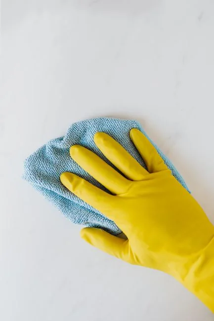 Hands in yellow gloves cleaning wall with sponge and spray bottle.